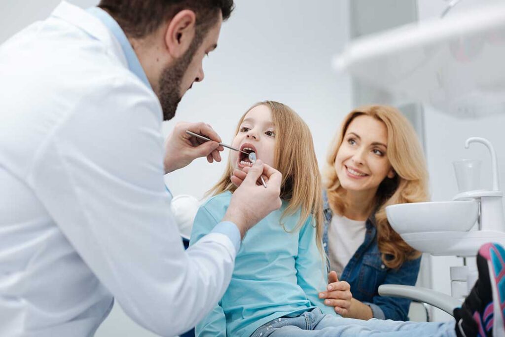 Person examining a swollen gum in a bathroom mirror beside a toothbrush and glass of water