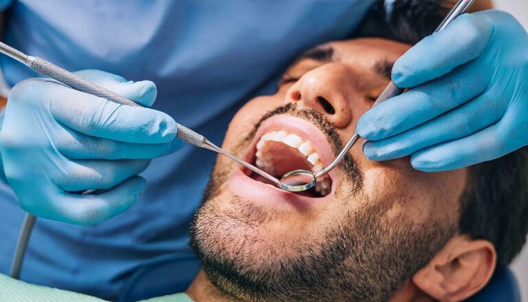 Person gently brushing teeth with a soft toothbrush beside a glass of water and sensitivity toothpaste.